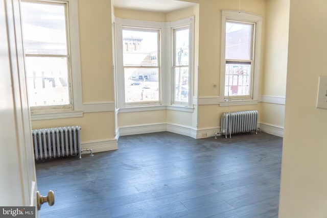 unfurnished room featuring radiator heating unit, a healthy amount of sunlight, and dark wood-type flooring