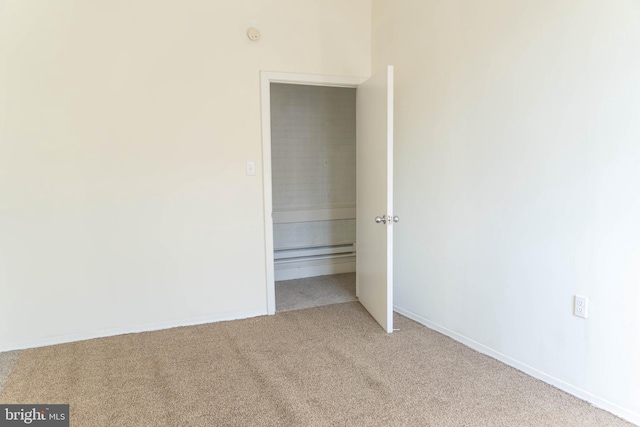 unfurnished bedroom featuring light carpet and a baseboard heating unit