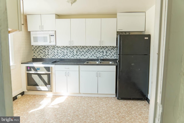 kitchen with oven, white cabinets, tasteful backsplash, black refrigerator, and sink