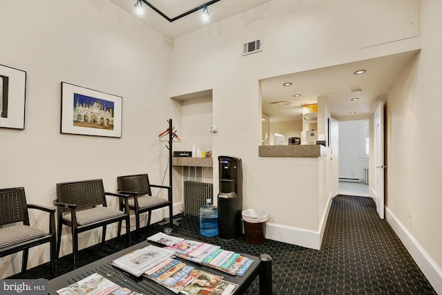 corridor with dark colored carpet, a towering ceiling, baseboard heating, and track lighting