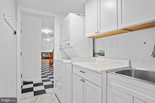 clothes washing area with cabinets, stacked washer and dryer, and sink