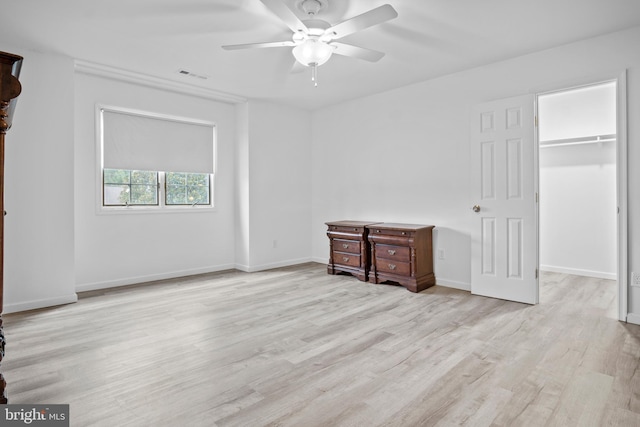 unfurnished bedroom featuring light hardwood / wood-style flooring, a closet, a walk in closet, and ceiling fan