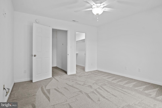 unfurnished bedroom featuring a spacious closet, light carpet, and ceiling fan