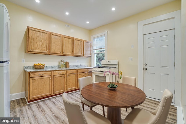 kitchen featuring light wood-type flooring, light stone counters, and white appliances