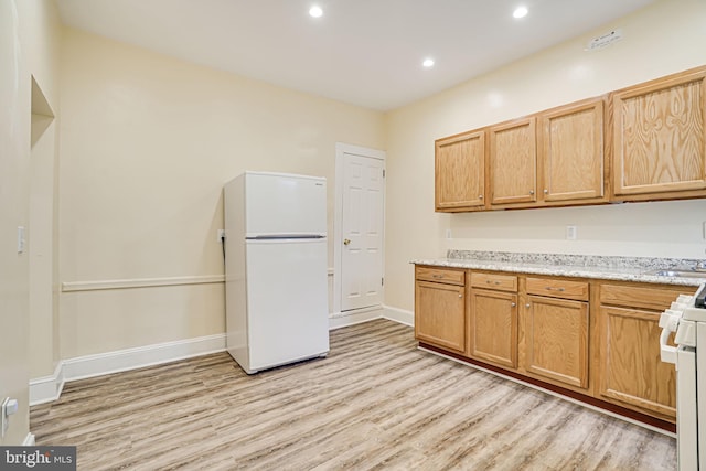 kitchen with white appliances, light stone countertops, and light wood-type flooring