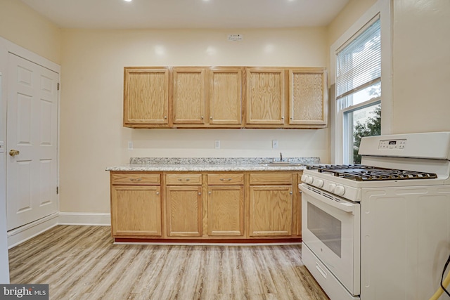 kitchen featuring white gas stove, light brown cabinetry, light stone countertops, and light hardwood / wood-style flooring