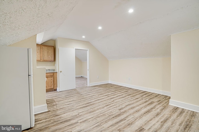 additional living space with vaulted ceiling, light wood-type flooring, and a textured ceiling