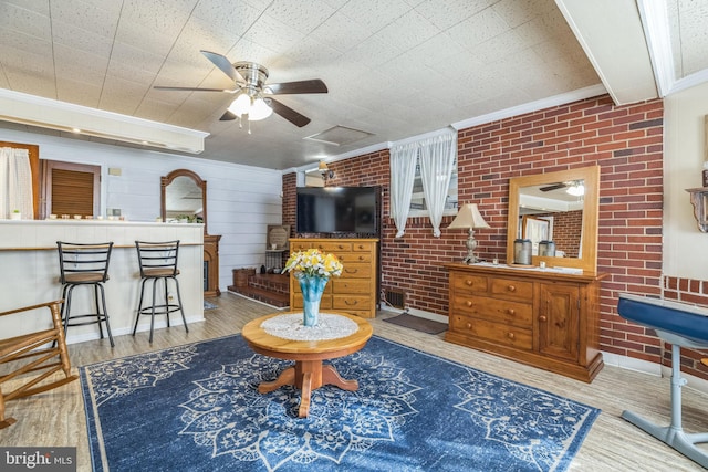 living room featuring ornamental molding, brick wall, light wood-type flooring, and ceiling fan