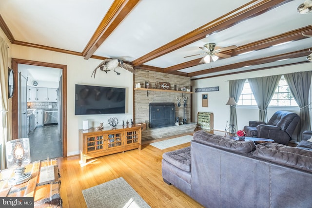 living room featuring ceiling fan, beam ceiling, a stone fireplace, crown molding, and light hardwood / wood-style floors