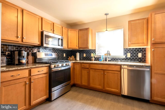 kitchen featuring pendant lighting, sink, backsplash, stainless steel appliances, and light wood-type flooring