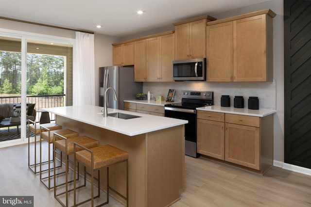 kitchen with stainless steel appliances, decorative backsplash, sink, an island with sink, and light hardwood / wood-style flooring