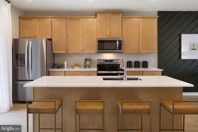 kitchen with an island with sink, light brown cabinetry, light wood-type flooring, and appliances with stainless steel finishes