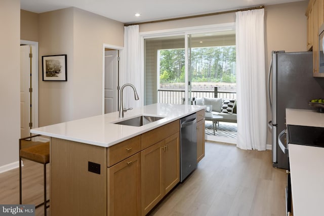 kitchen with stainless steel appliances, a center island with sink, sink, a kitchen breakfast bar, and light hardwood / wood-style flooring