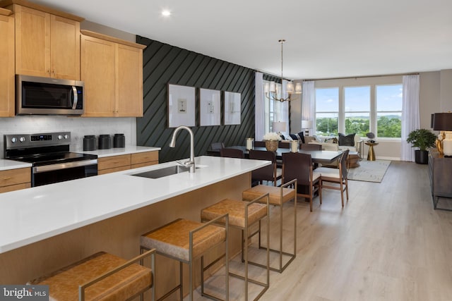 kitchen featuring stainless steel appliances, hanging light fixtures, sink, a breakfast bar area, and light hardwood / wood-style flooring