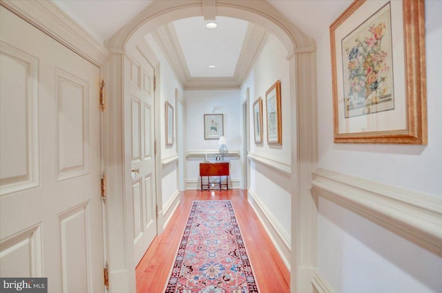 corridor featuring hardwood / wood-style flooring, a raised ceiling, and ornamental molding