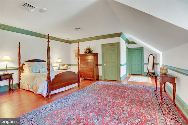 bedroom featuring wood-type flooring, vaulted ceiling, and crown molding