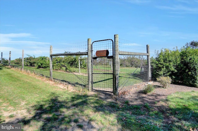 view of gate featuring a lawn and a rural view