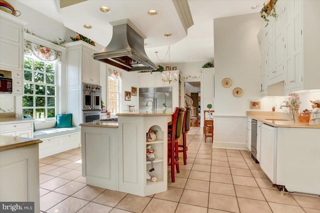 kitchen with white cabinetry, dishwasher, multiple ovens, island exhaust hood, and light tile patterned flooring