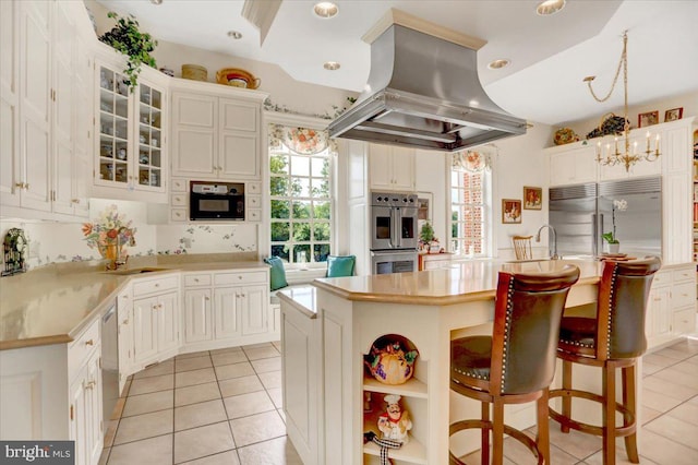 kitchen with a breakfast bar, an island with sink, island range hood, white cabinetry, and stainless steel appliances