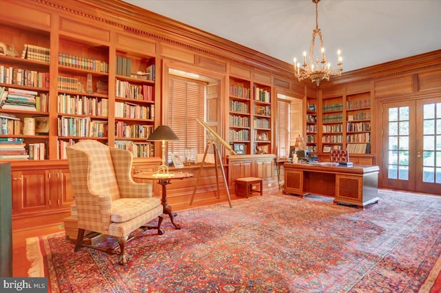 office space featuring french doors, built in shelves, wooden walls, crown molding, and an inviting chandelier