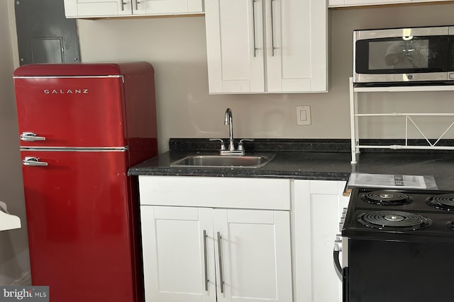 kitchen with black range with electric stovetop, refrigerator, white cabinetry, and sink