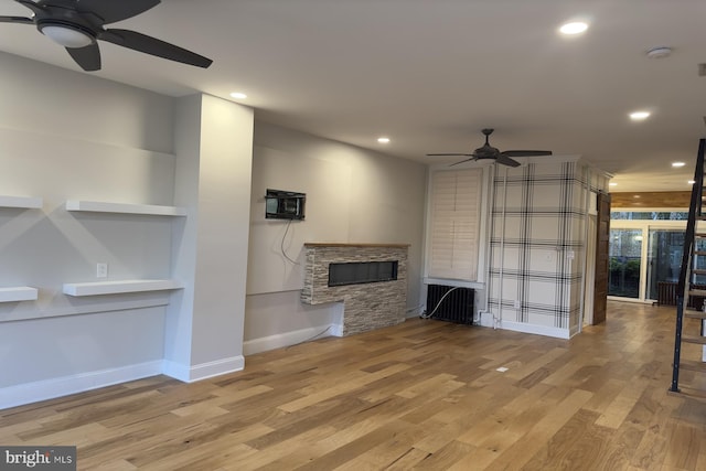 unfurnished living room with ceiling fan, an AC wall unit, a fireplace, and light hardwood / wood-style flooring