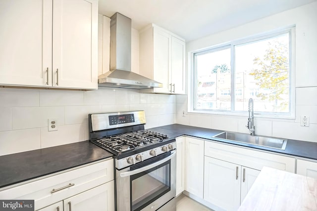 kitchen featuring wall chimney range hood, stainless steel gas range, sink, white cabinetry, and tasteful backsplash