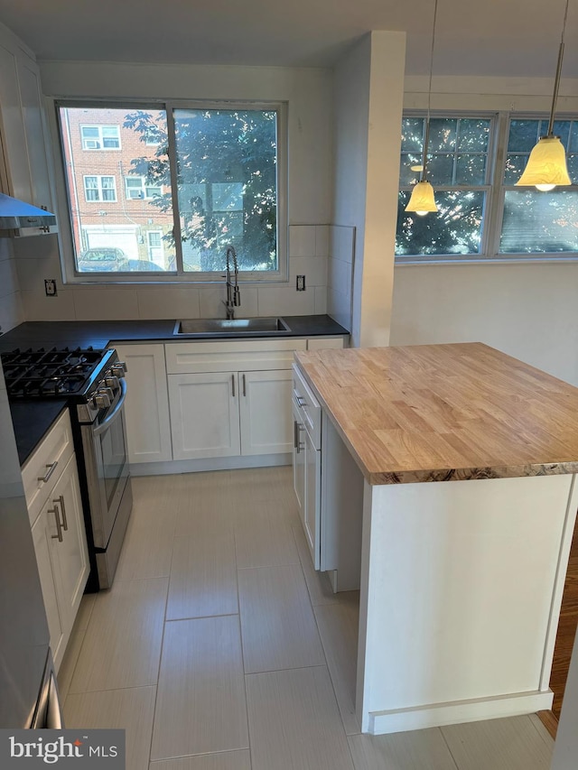 kitchen featuring white cabinets, backsplash, sink, decorative light fixtures, and stainless steel gas range