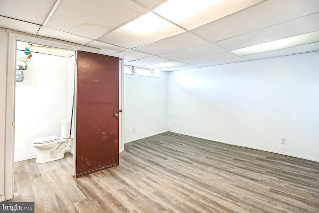 below grade area with a drop ceiling, wood finished floors, and baseboards