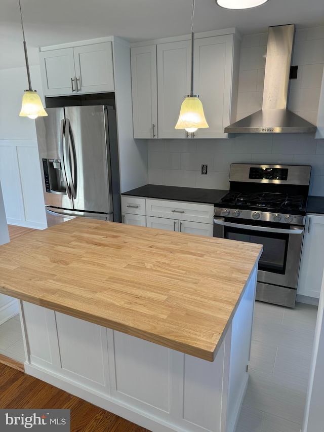 kitchen with wall chimney range hood, decorative backsplash, white cabinets, appliances with stainless steel finishes, and pendant lighting