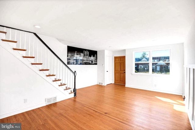 unfurnished living room with stairway, wood finished floors, visible vents, and baseboards