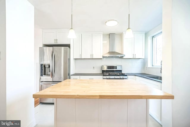 kitchen featuring butcher block countertops, appliances with stainless steel finishes, wall chimney range hood, and decorative backsplash