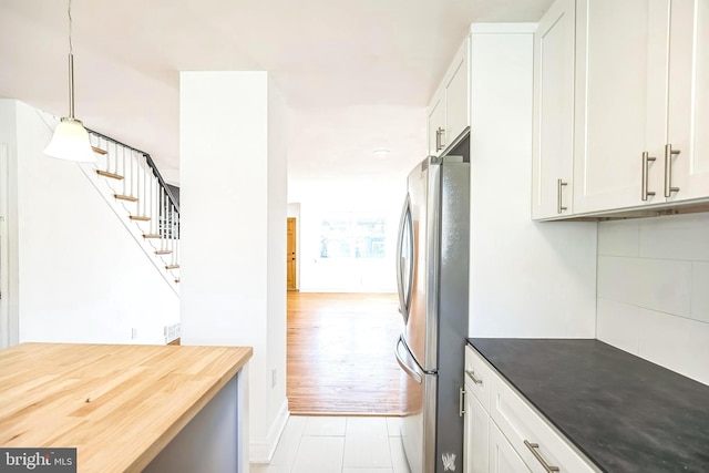 kitchen with light tile patterned floors, baseboards, hanging light fixtures, white cabinets, and freestanding refrigerator