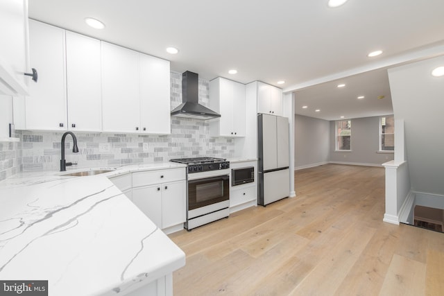 kitchen featuring wall chimney range hood, backsplash, gas range oven, sink, and white refrigerator