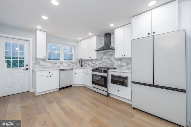 kitchen featuring white appliances, light hardwood / wood-style flooring, wall chimney range hood, and white cabinetry