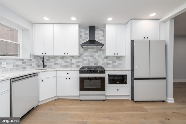 kitchen featuring white appliances, wall chimney range hood, sink, decorative backsplash, and light hardwood / wood-style flooring