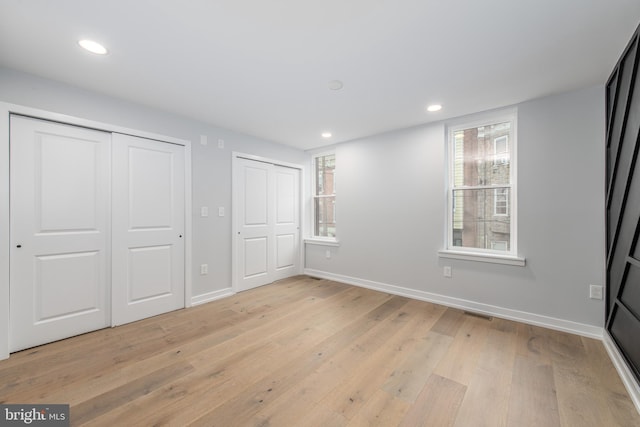 unfurnished bedroom with multiple closets and light wood-type flooring