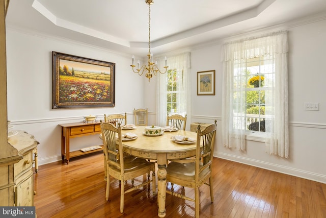 dining space featuring an inviting chandelier, wood-type flooring, ornamental molding, and a raised ceiling