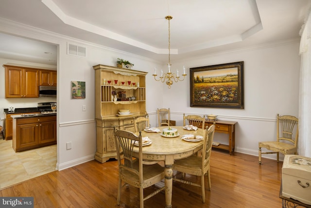 dining space with an inviting chandelier, ornamental molding, light hardwood / wood-style floors, and a raised ceiling