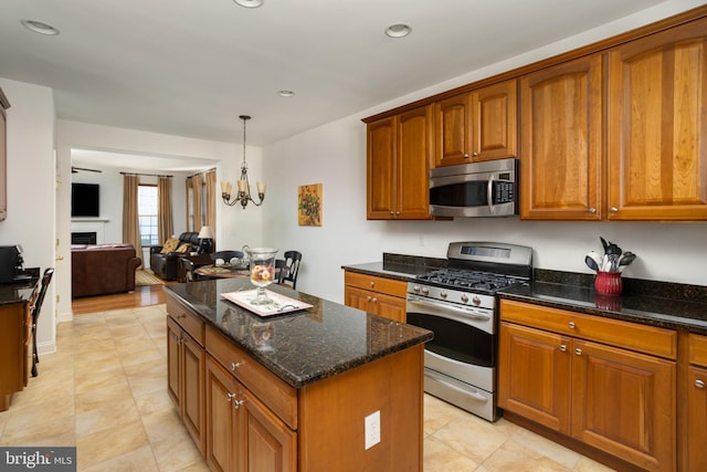 kitchen featuring appliances with stainless steel finishes, an inviting chandelier, a center island, decorative light fixtures, and dark stone counters