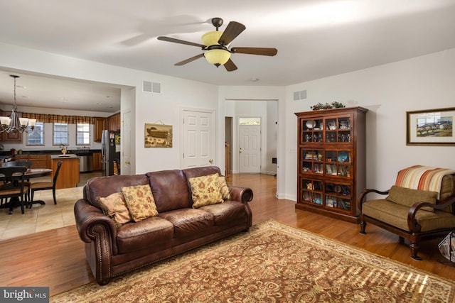 living room with ceiling fan with notable chandelier and light wood-type flooring