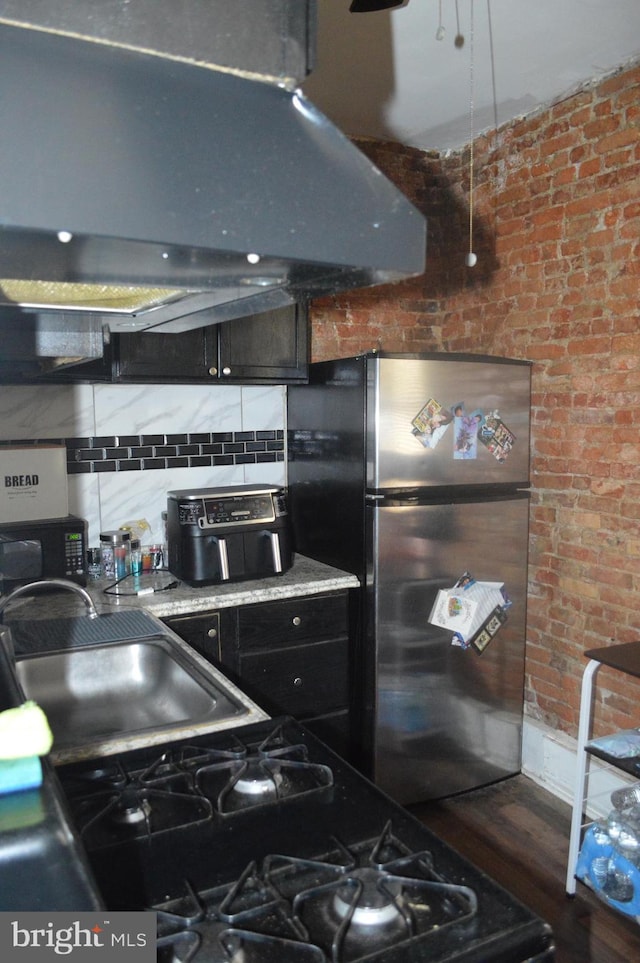 kitchen with decorative backsplash, dark hardwood / wood-style floors, range hood, brick wall, and stainless steel refrigerator