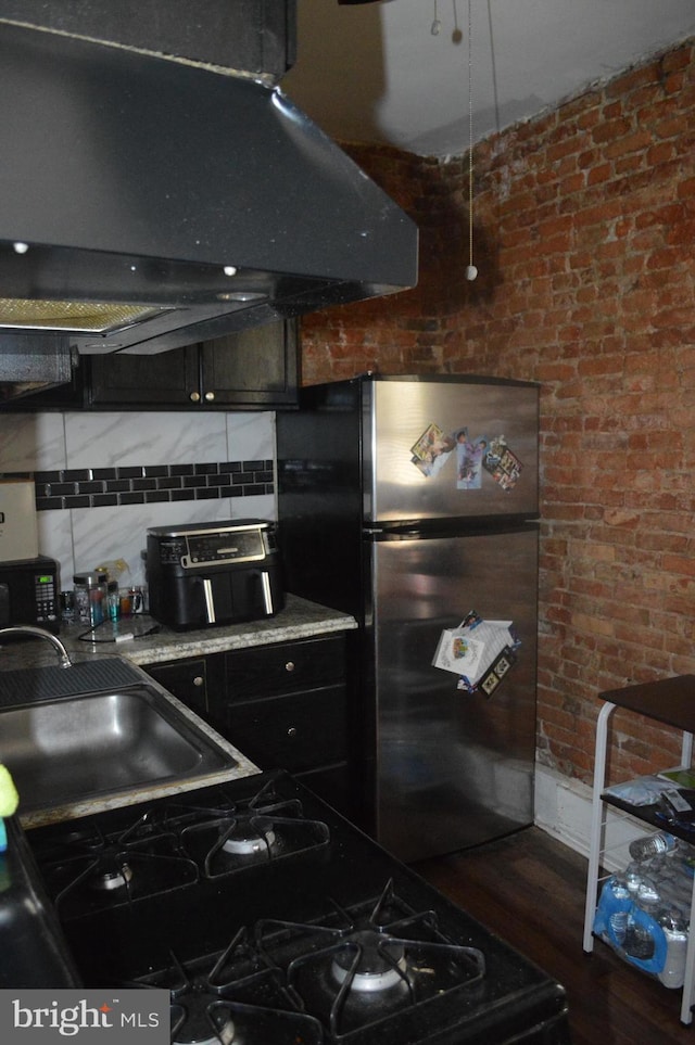 kitchen with decorative backsplash, dark wood-type flooring, brick wall, ventilation hood, and stainless steel refrigerator