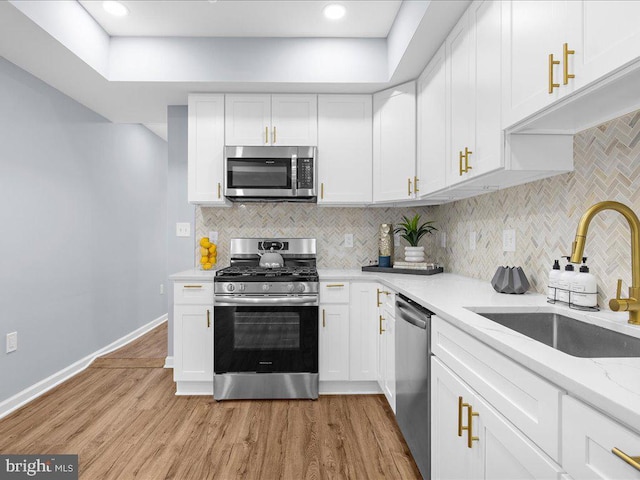 kitchen with light stone counters, sink, light hardwood / wood-style flooring, white cabinetry, and appliances with stainless steel finishes