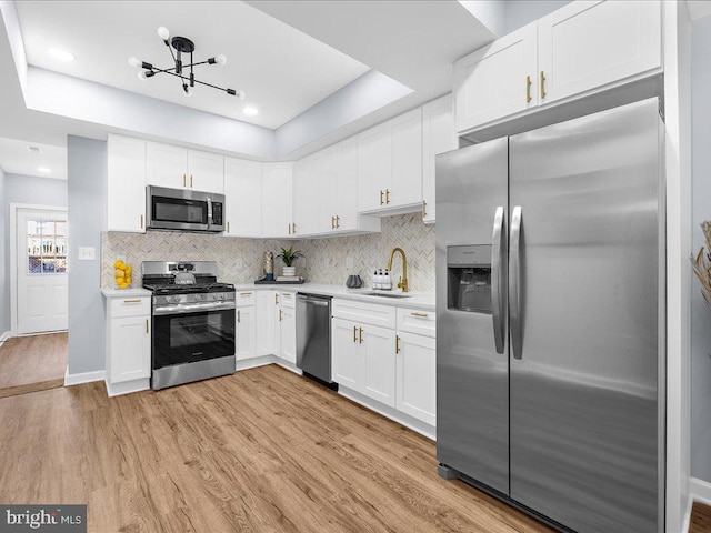 kitchen with sink, white cabinetry, a tray ceiling, appliances with stainless steel finishes, and light wood-type flooring