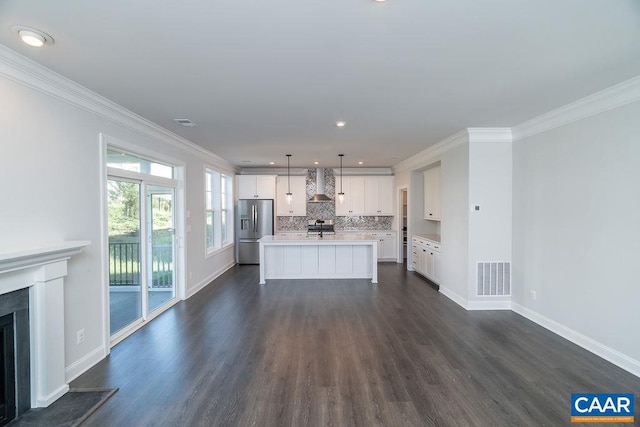 kitchen with stainless steel fridge, a kitchen island, decorative light fixtures, wall chimney exhaust hood, and white cabinetry