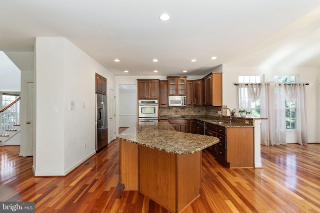 kitchen featuring backsplash, appliances with stainless steel finishes, dark stone counters, dark hardwood / wood-style floors, and sink