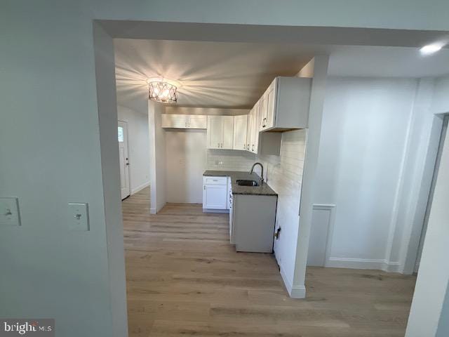 kitchen with sink, backsplash, white cabinetry, an inviting chandelier, and light hardwood / wood-style floors