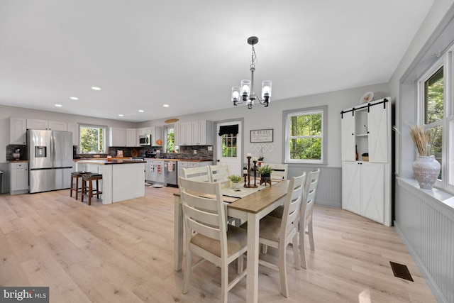 dining space featuring plenty of natural light, a barn door, a chandelier, and light hardwood / wood-style floors