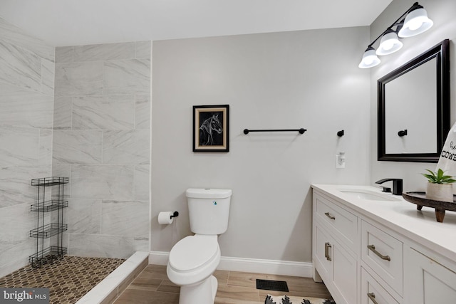 bathroom with a tile shower, hardwood / wood-style floors, vanity, and toilet